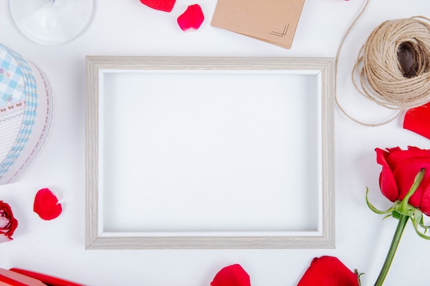 Top view of an empty picture frame with a gift box ball of rope red color roses small postcard on white background with copy space