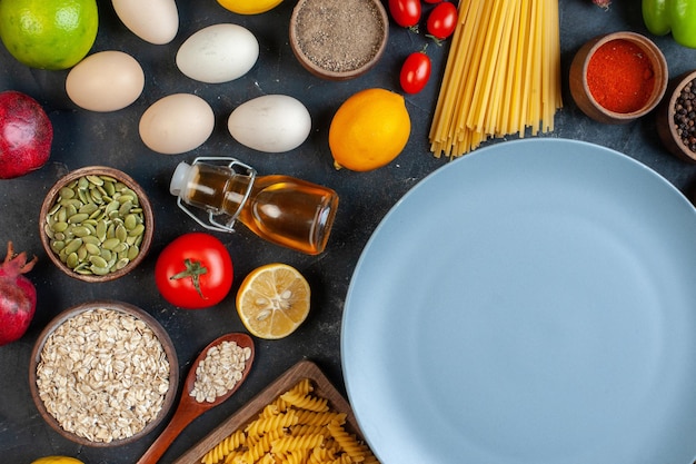 Вид сверху пустая тарелка вокруг яиц, помидоров, приправ и итальянской пасты на темном фоне, цветная еда, еда, овощная кухня, кухня