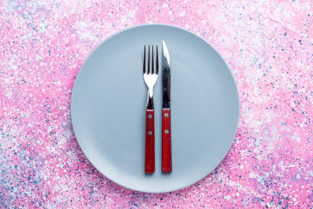 Top view empty plate blue colored with fork and knife on bright pink wall color photo plate food cutlery