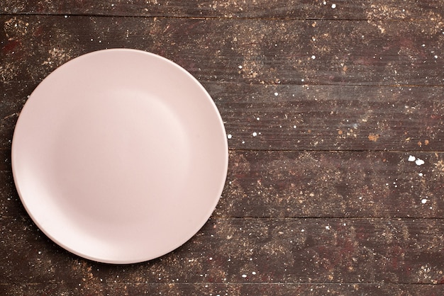 Top view of empty plate pinked on brown rustic, wooden desk, food cutlery