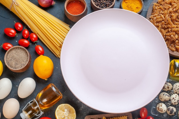 Вид сверху пустая тарелка с сырыми пастами, овощными приправами и яйцами на темном столе