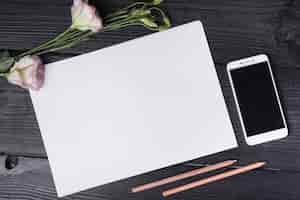 Free photo top view of eustoma flower; blank white paper; colored pencils and cell phone on wooden desk