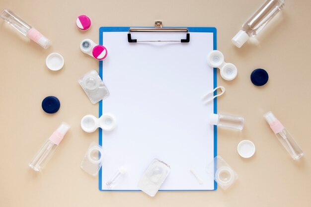 Top view eye care accessories on beige background with clipboard mock-up