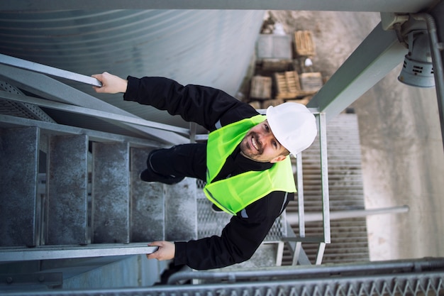 Top view of factory worker climbing metal stairs on industrial silo building