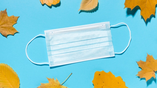 Top view of fall leaves with medical mask