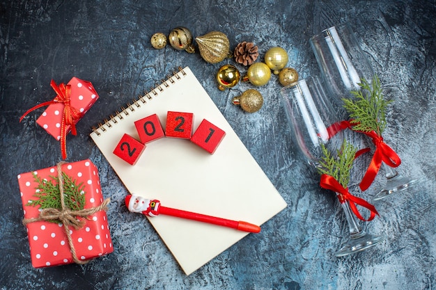 Top view of fallen glass goblets with red ribbon and decoration accessories next to gift boxes on dark background