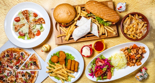 Top view fast food mix hamburger doner sandwich chicken nuggets rice vegetable salad chicken sticks caesar salad mushrooms pizza chicken ragout french fries mayo a