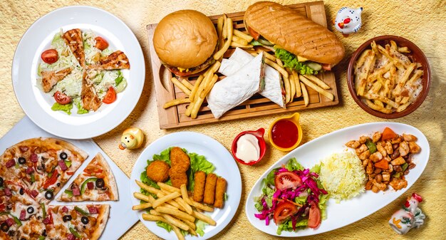 Top view fast food mix hamburger doner sandwich chicken nuggets rice vegetable salad chicken sticks caesar salad mushrooms pizza chicken ragout french fries mayo a