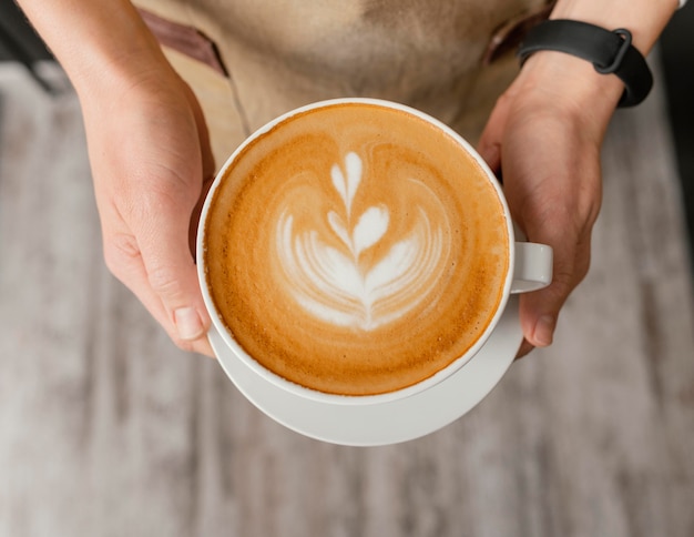 Top view of female barista holding decorated cup of coffee in hands