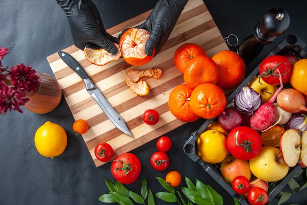 Top view female cook cleaning tangerines on dark surface