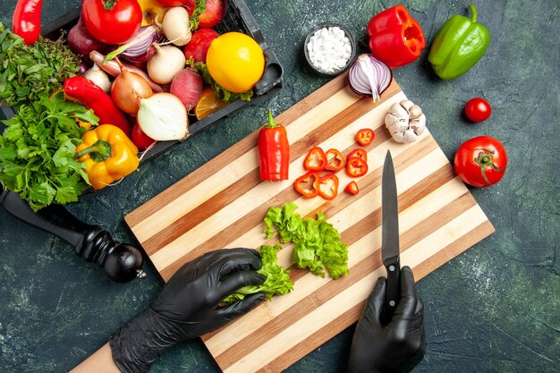 Top view female cook cutting fresh green salad on a gray surface