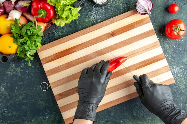 Top view female cook cutting red hot pepper on gray surface