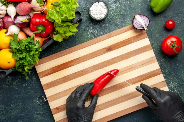 Top view female cook cutting red hot pepper on the gray surface