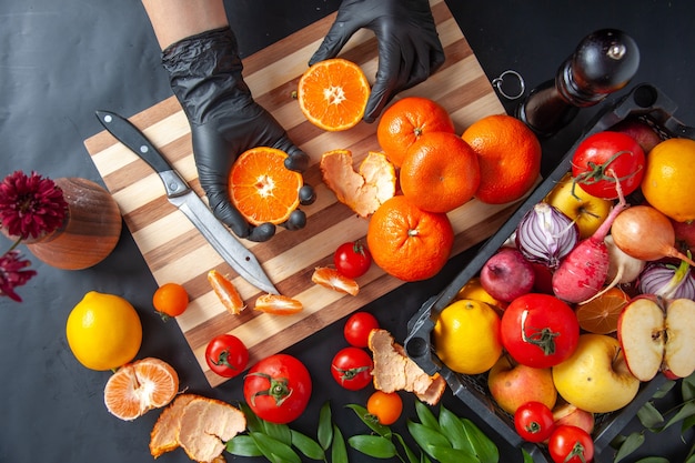 Top view female cook holding half sliced tangerines on a gray surface