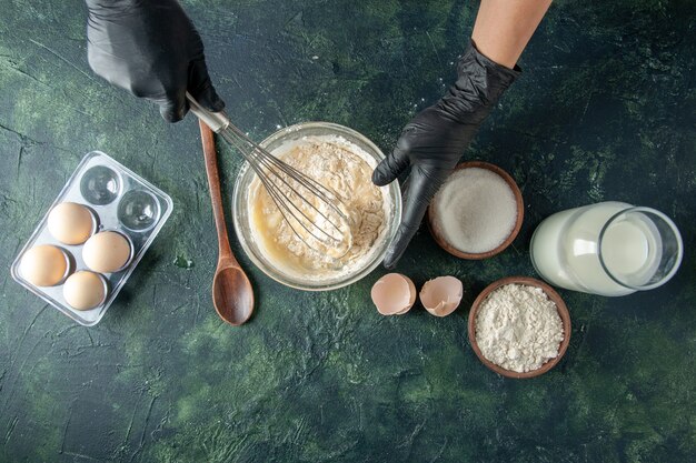 Top view female cook mixing up flour in plate with eggs on a dark surface