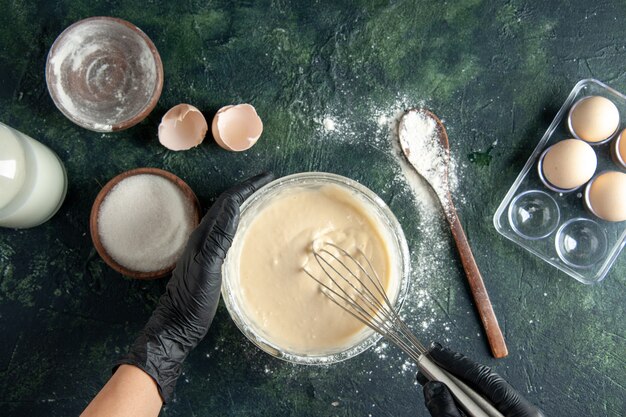 Top view female cook mixing up ingredients and making dough on dark surface