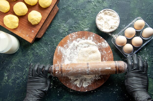 Top view female cook rolling out dough with flour on a dark surface