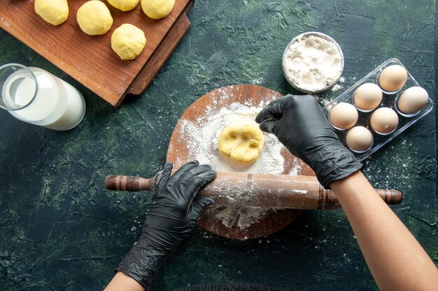 Top view female cook rolling out dough with flour on dark surface