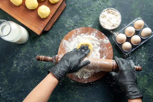 Top view female cook rolling out dough with flour on dark surface