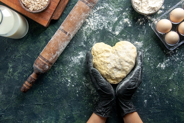 Free photo top view female cook working with heart shaped dough on dark gray surface