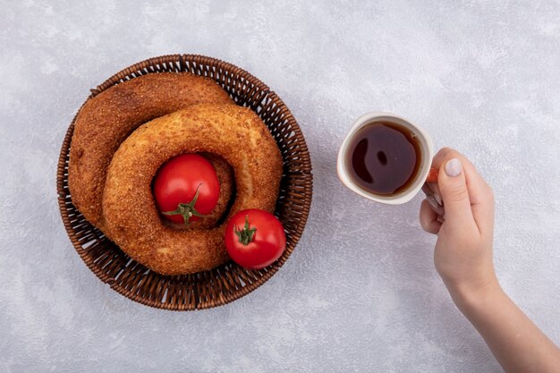 白い背景の上のトルコのベーグルのバケツとお茶のカップを持っている女性の手の上面図