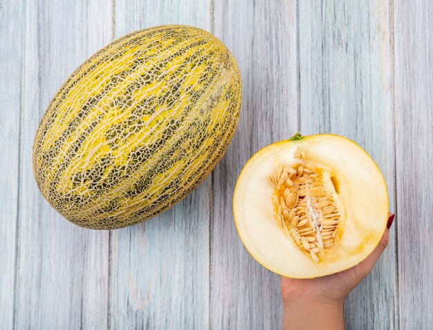 Top view of female hand holding fresh and delicious cantaloupe melon on grey wood