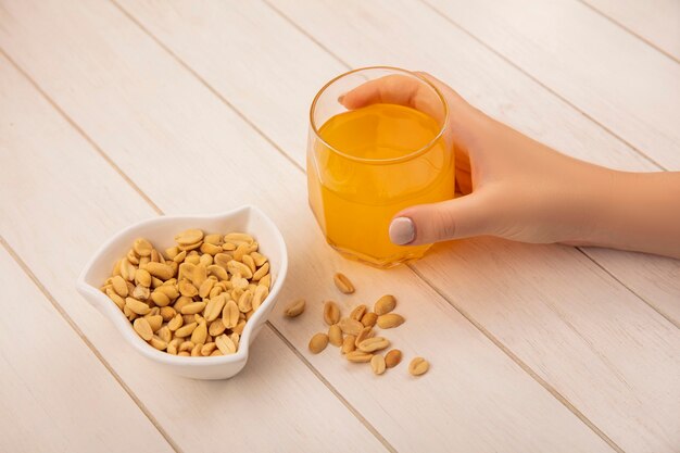 Top view of female hand holding a glass of orange juice with pine nuts on a bowl on a beige wooden table