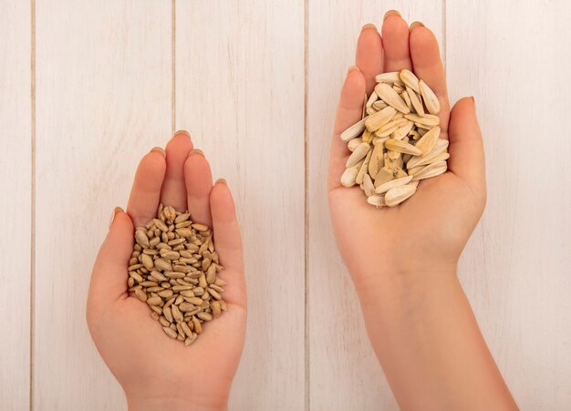 Top view of female hand holding in one hand tasty salty white sunflower seeds and in the other hand shelled sunflower seeds on a beige wooden table