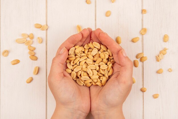 Top view of female hand holding tasty salty pine nuts on a beige wooden table