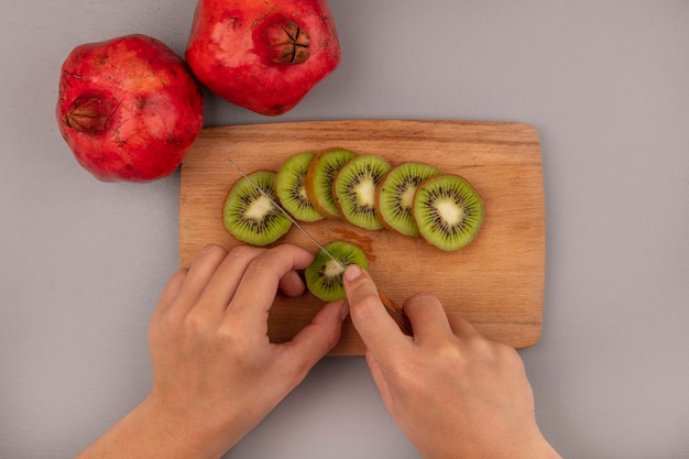 Top view of female hands cutting fresh kiwi on a wooden kitchen board with knife with pomegranates isolated