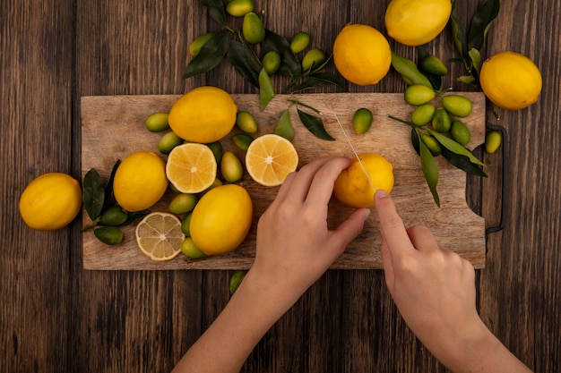 Top view of female hands cutting fresh lemons on a wooden kitchen board with knife with kinkans isolated on a wooden surface