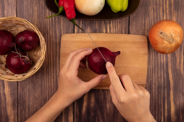 Top view of female hands cutting a fresh red onion on a wooden kitchen board with knife on a wooden wall