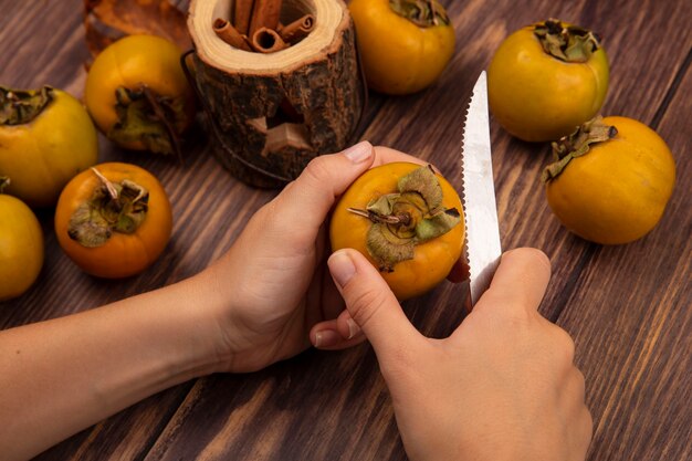 top view of female hands cutting persimmon fruit on a wooden table