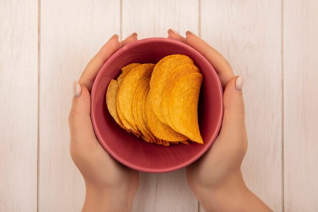 베이지 색 나무 테이블에 맛있는 바삭한 칩 한 그릇을 들고 여성 손의 상위 뷰