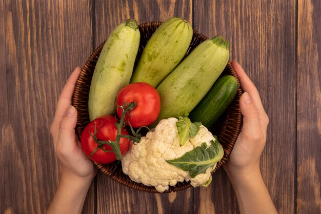 나무 벽에 호박 토마토 오이와 콜리 플라워와 같은 신선한 야채 양동이를 들고 여성 손의 상위 뷰