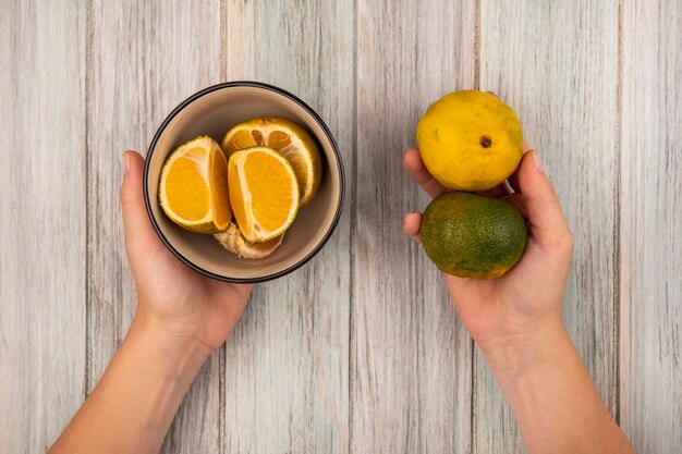 Top view of female hands holding a citrus fruit tangerines on a grey wooden wall