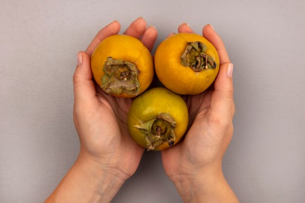 Top view of female hands holding fresh organic persimmon fruits