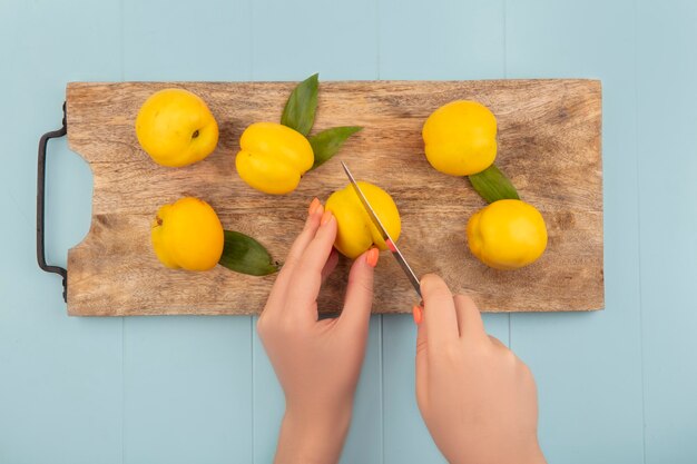 Top view of female hands holding fresh yellow peach on a wooden kitchen board on a blue background