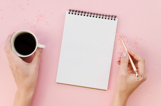 Top view of female hands holding mug and pen