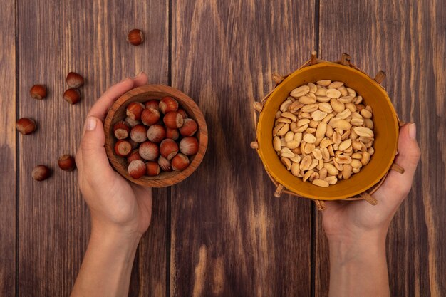 Free photo top view of female hands holding a wooden bowl of peanuts and peanuts on a bucket on a wooden wall