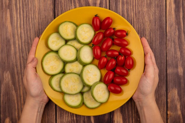 나무 표면에 토마토와 호박과 같은 신선한 야채의 노란색 접시를 들고 여성 손의 상위 뷰