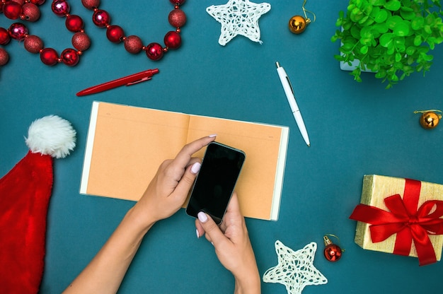 The top view of female hands with phone and Christmas decorations