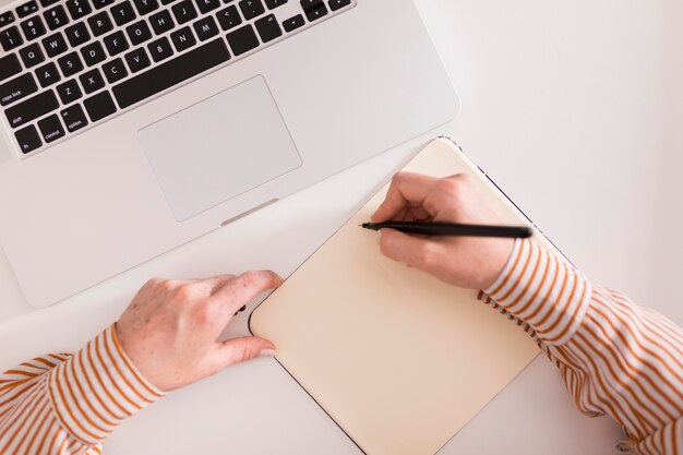 Top view of female teacher writing something and using laptop during online class