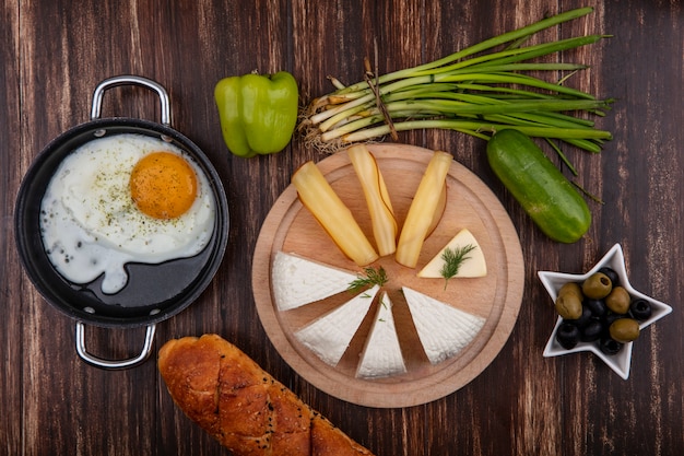 Top view feta cheese with smoked cheese on a stand with olives  green peppers  cucumber and eggs on a wooden background