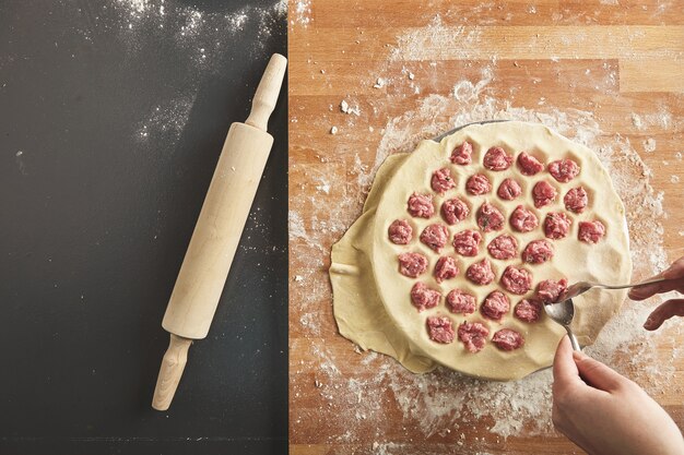 Top view filling dumplings mold with minced meat. All isolated on old vintage table and wooden board. Rolling pin near. Step by step guide cooking ravioli or pelmeny