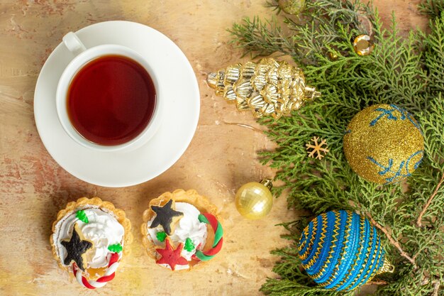 상위 뷰 전나무 가지 크리스마스 트리 장식 컵 케이크 베이지색 배경에 차 한 잔