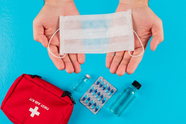 Top view first aid kit in hands with mask, vial, pills and bottle. horizontal