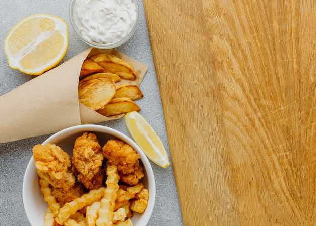 Free photo top view of fish and chips in bowl and paper wrap with copy space and lemon