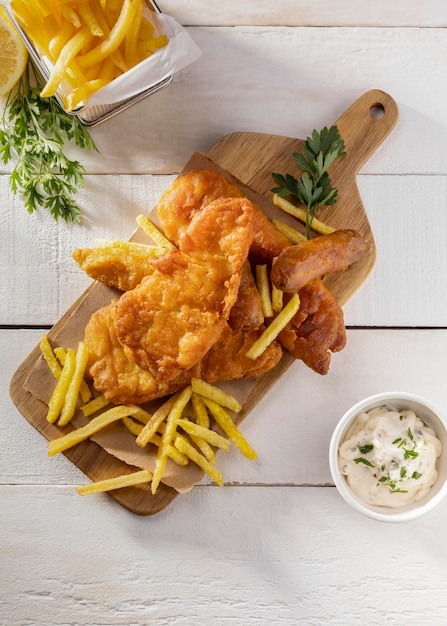 Top view of fish and chips on chopping board with sauce