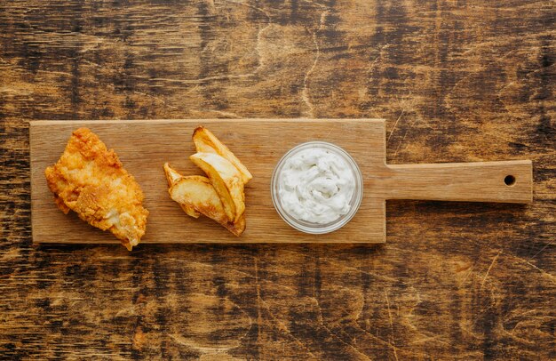 Top view of fish and chips on chopping board with sauce